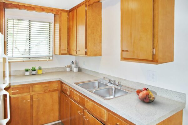 Rendering of a kitchen with wood cabinets, gray countertops, a white fridge, and a window.