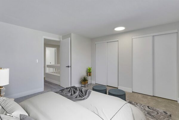Bedroom with two closet doors, tan carpet, a bed with plush blankets, and plants.