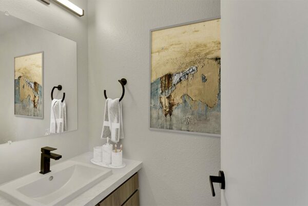 Bathroom with white walls, white countertops, white cabinets, and art work.