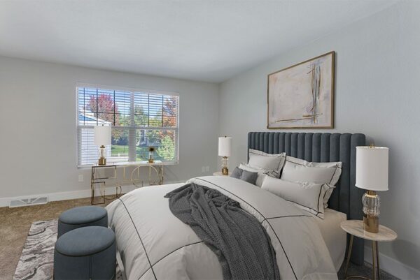 Bedroom with tan carpet, a large window, and a bed with plush blankets.