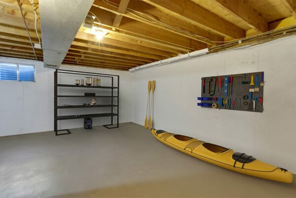 Unfinished basement with storage shelves, tools handing on a wall, and a kayak.