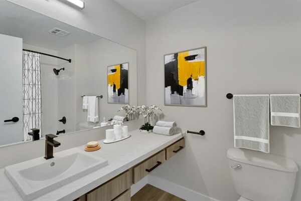 Bathroom with white countertops, wood cabinets, and a full shower with black fixtures.