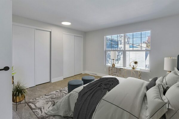 Bedroom with tan carpet, white walls, a large window, and two closet doors.