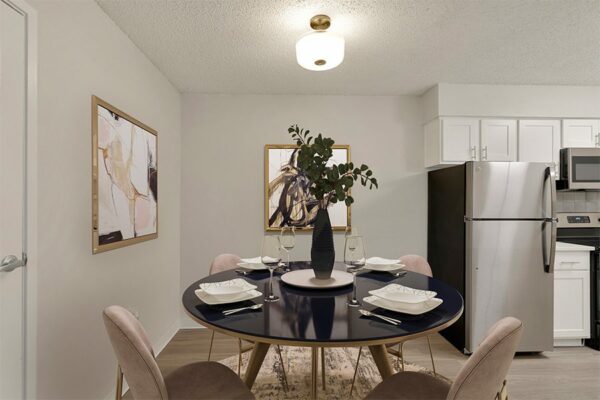 Dining area with a carpet over wood floors, art work on the walls, and a view into the kitchen with stainless steel appliances.