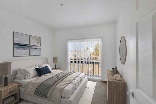 Bedroom with carpet, plush bed with headboard, bedside tables with lamps, and sliding balcony door.