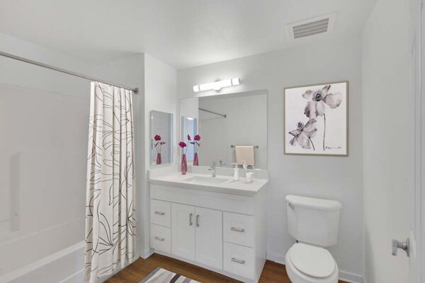 Trocadero apartment bathroom with white cabinet, white counter, tiled shower tub, and mirror.