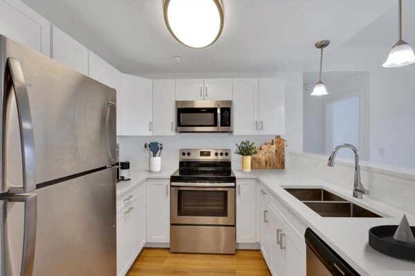Trocadero apartment kitchen with wood style floor, white cabinets and counters, and stainless steel appliances.