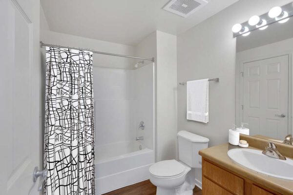 Trocadero apartment bathroom with wood style floor and cabinets, large mirror, and tiled shower tub.