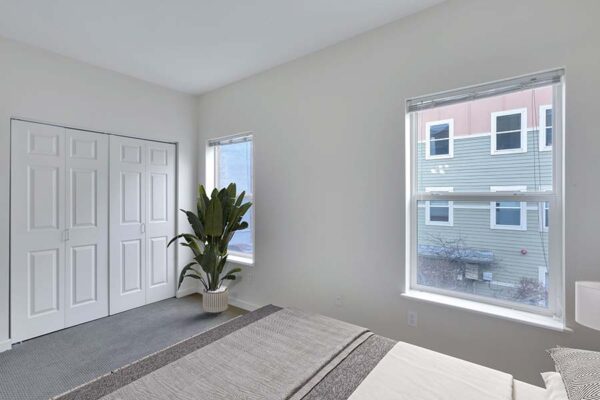 Trocadero apartment bedroom with plush bed, potted plant, large closet, and large windows.