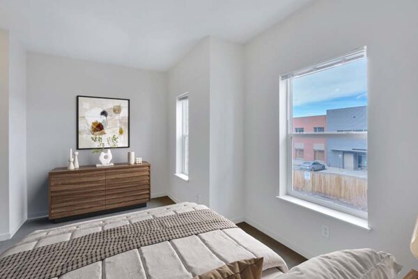 Trocadero apartment bedroom with plush bed, dresser with decor, framed artwork, and large windows.