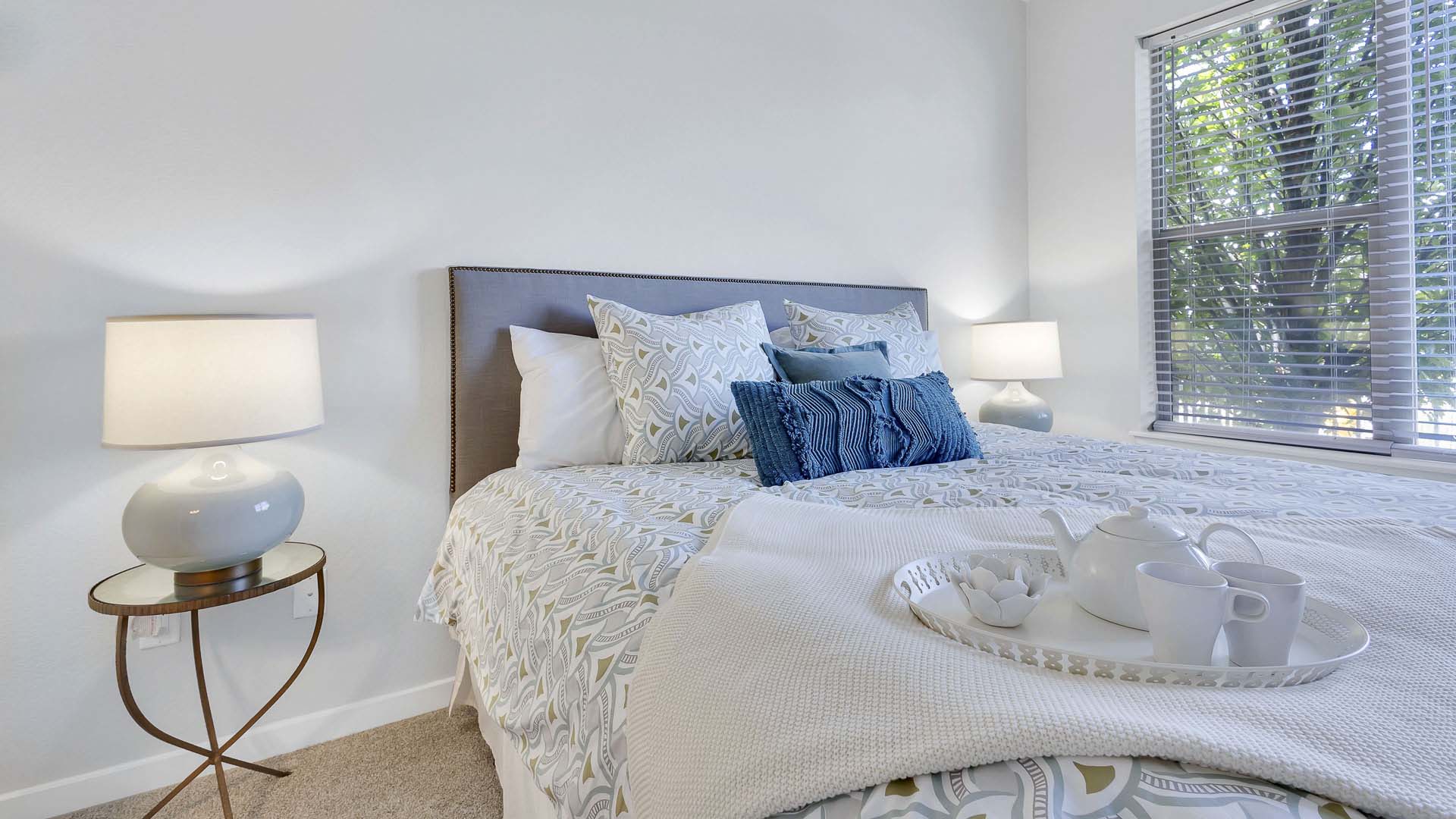 Monaco Row apartment bedroom with plush bed, bedside tables with lamps, and large window.