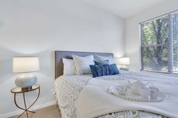 Monaco Row apartment bedroom with plush bed, bedside tables with lamps, and large window.