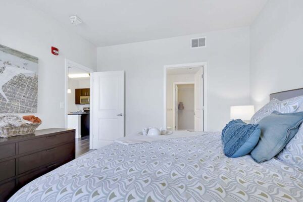 Monaco Row apartment bedroom with plush bed, dresser, and bathroom door.