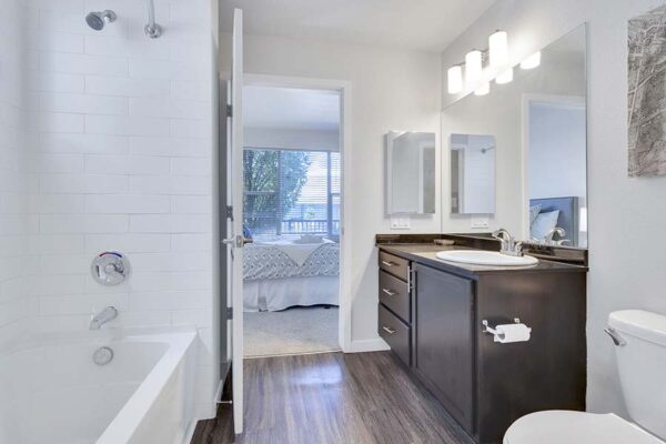 Monaco Row apartment bathroom with wood style floor, dark counters, and tiled shower tub.