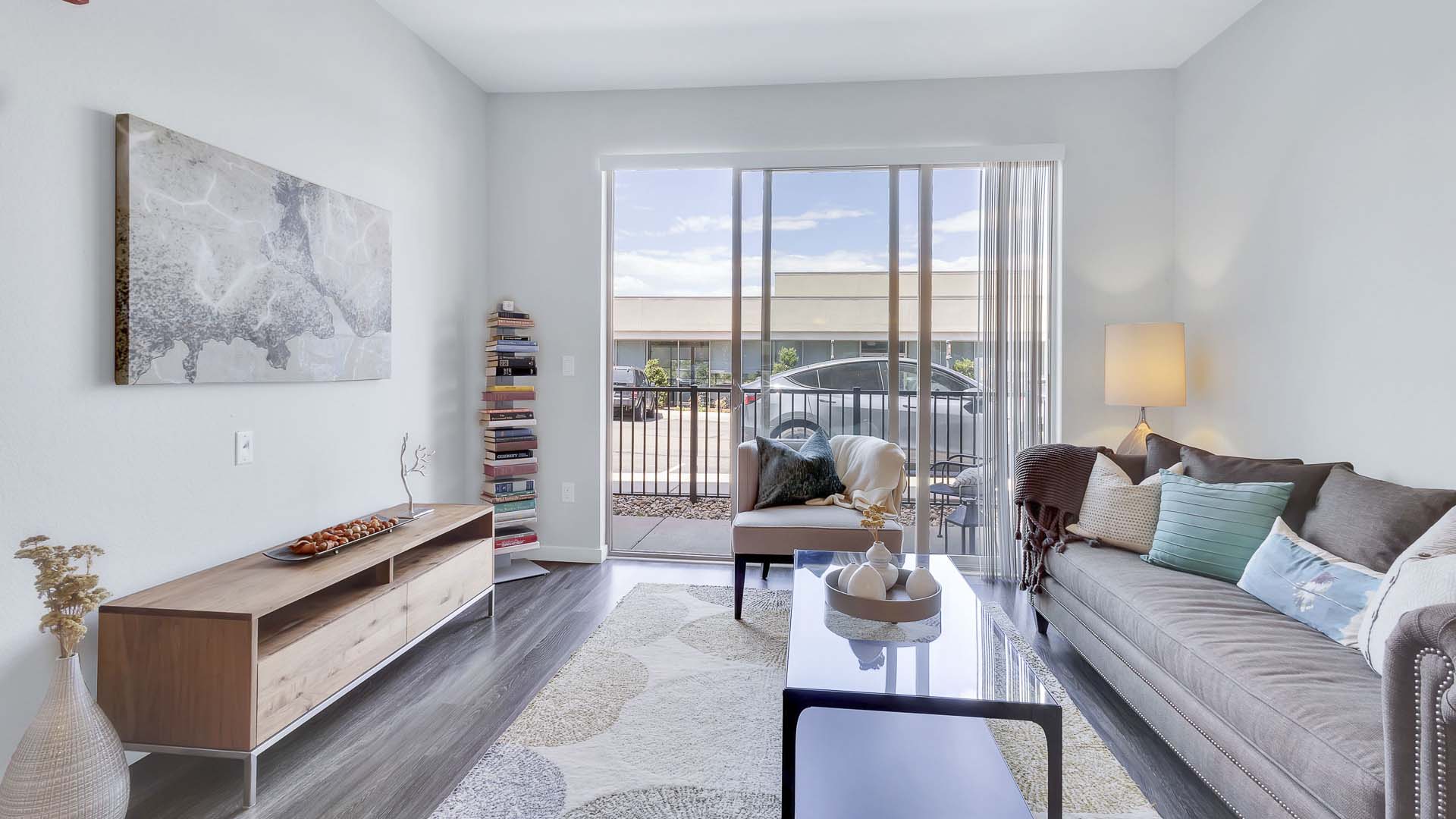 Monaco Row apartment living room with plush seating, bookshelf, and balcony door.