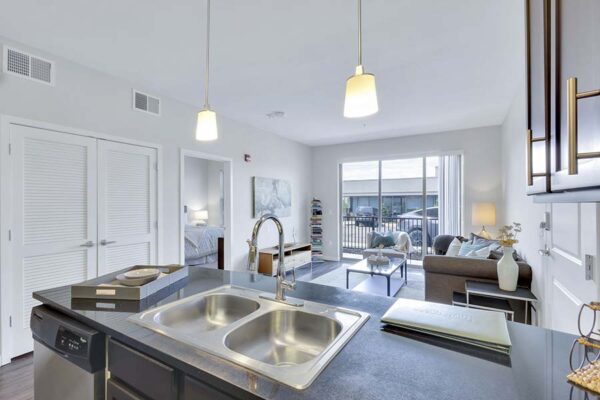 Monaco Row apartment kitchen with wood style floor and cabinets, dark counters, and stainless steel appliances.
